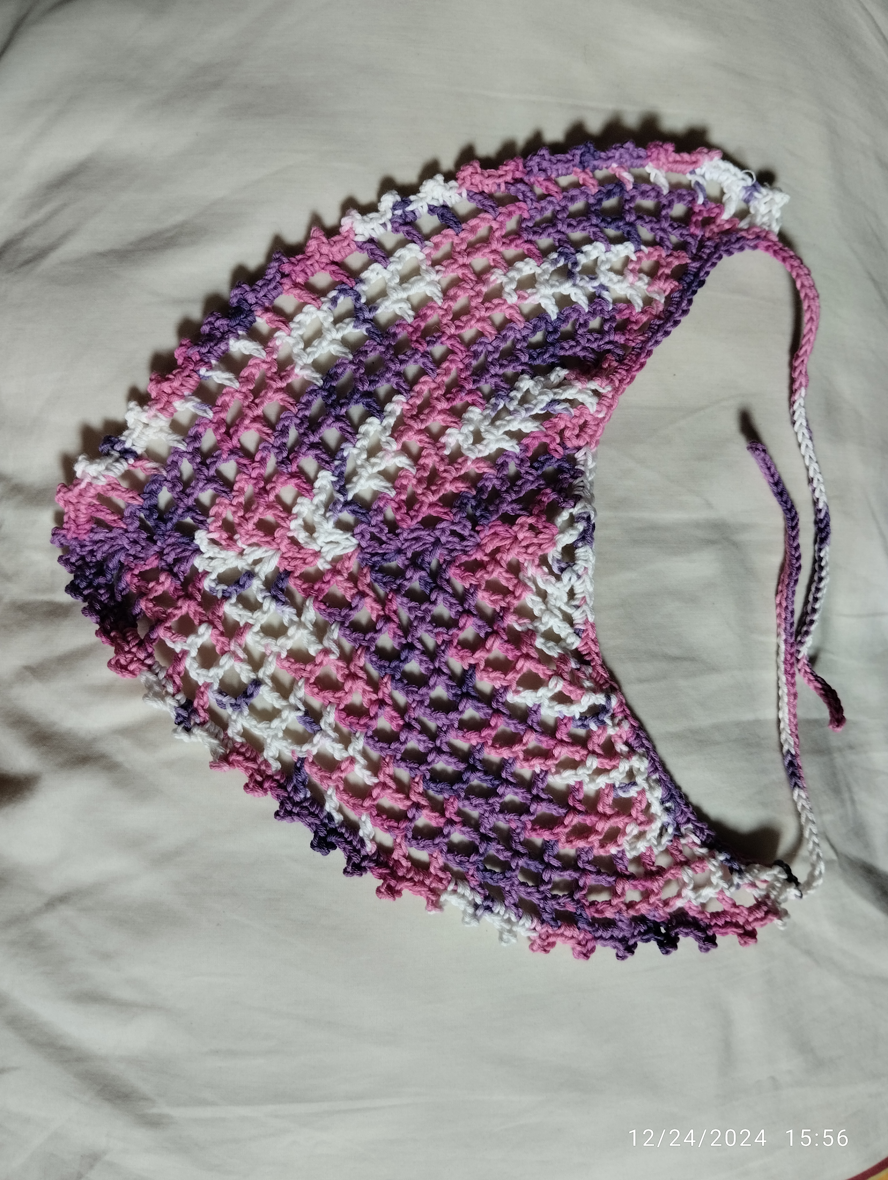 a triangle headscarf made with multicolored yarn with whites, pinks, and purples.